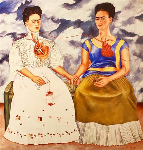 The Two Fridas by Frida Kahlo, 1939. This double self-portrait shows two different versions of Kahlo sitting side by side, holding hands against a stormy, gray background. On the left, one Frida wears a traditional white European-style dress, with her heart exposed and a damaged artery connecting to a pair of scissors, symbolizing her emotional pain and conflicting feelings involving her self identity. On the right, the second Frida is dressed in a vibrant Mexican Tehuana outfit, with her heart intact and holding a small portrait of Diego Rivera, her husband, representing her connection to her Mexican heritage and her love.